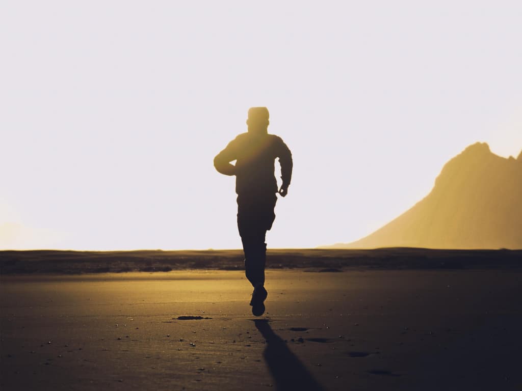 praticante de corrida em silhueta treinando durante o "golden hour" (final de tarde), ilustrando um dos horários de pico de performance física.