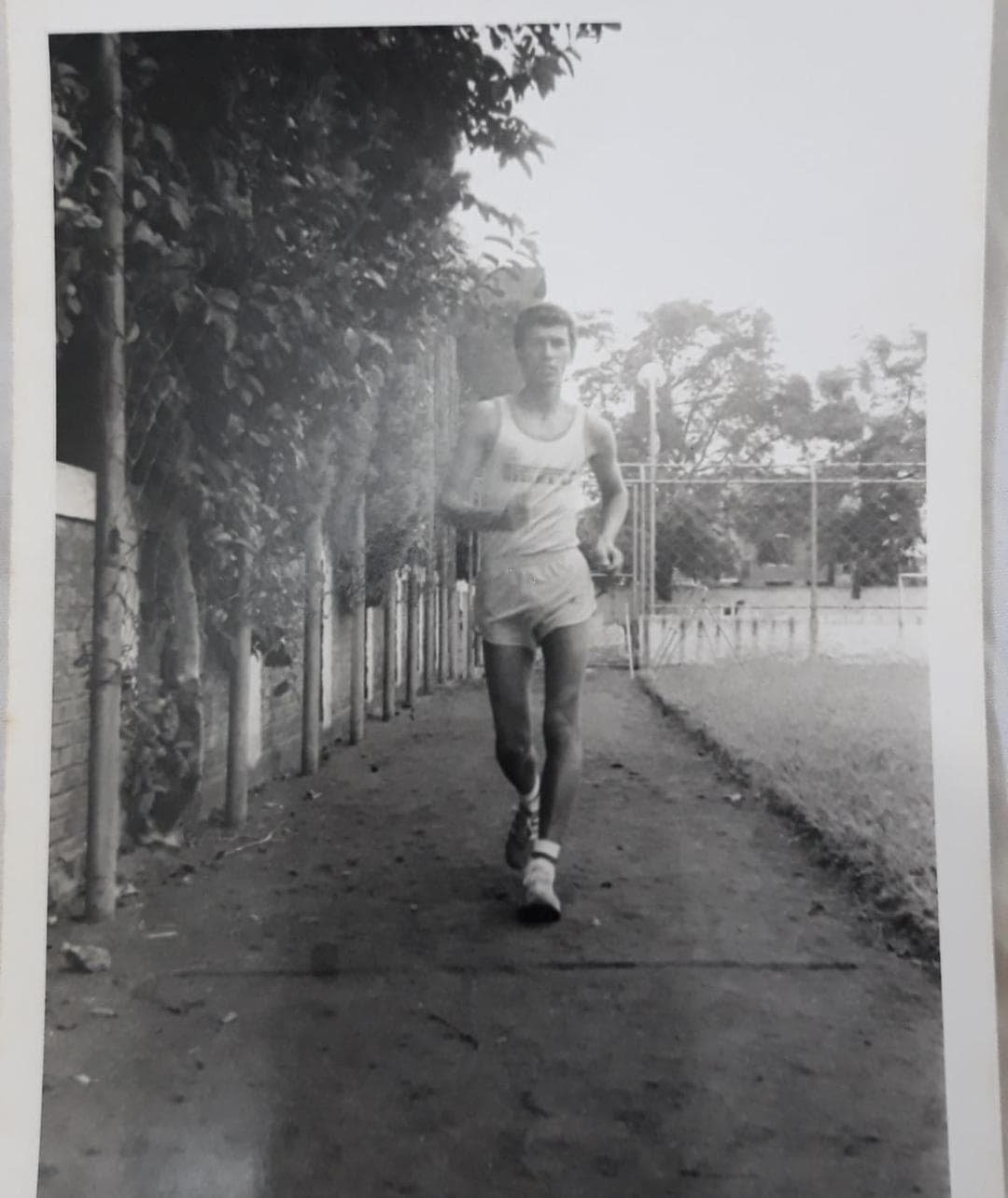 Fotografia capturando o treinador Claudio Bertolino em sua rotina de treino no início da carreira esportiva, de forma dedicada e focada em um pequeno percurso de pedrisco que contornava um campo de futebol.